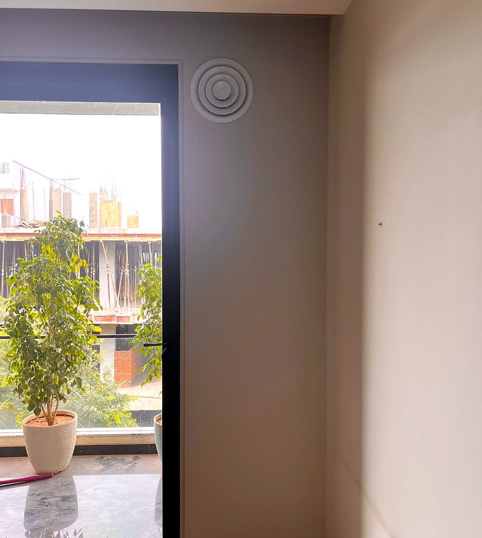 A round diffuser high on an indoor wall, beside a glass door to a balcony