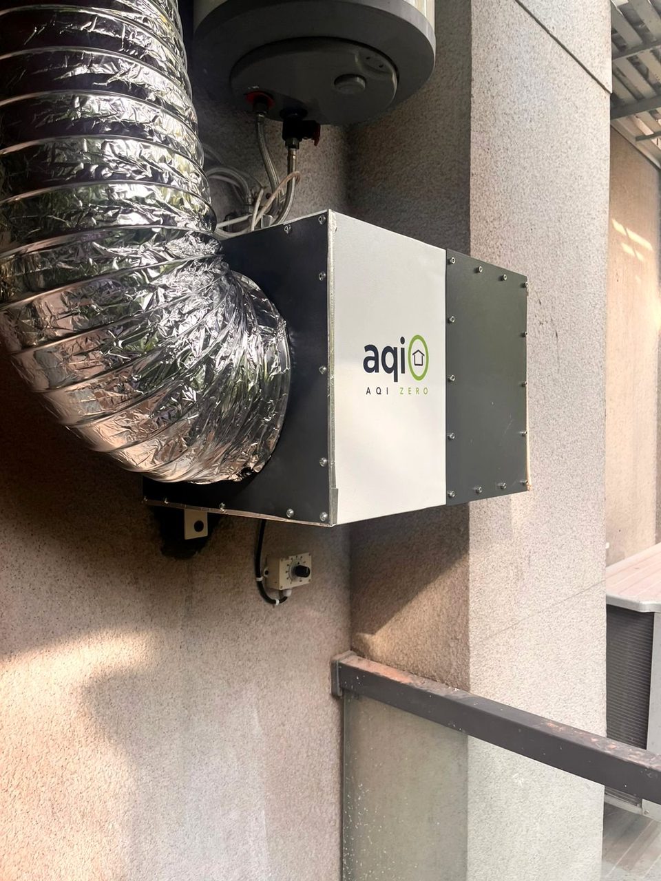 An aqi0 unit mounted on an outside wall, with its flexible silver duct curving up out of frame